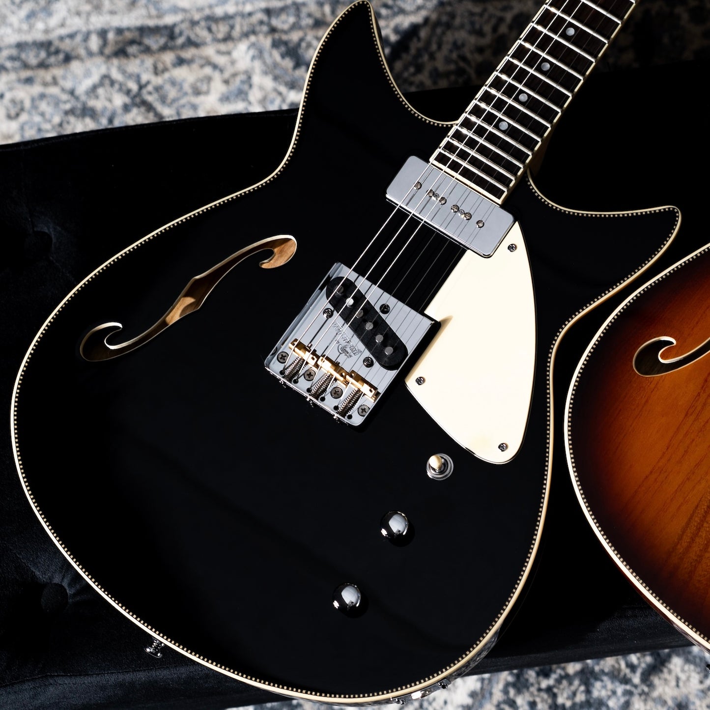 A close-up of a black Duocata guitar with checkerboard trim, a cream pickguard, and chrome hardware.
