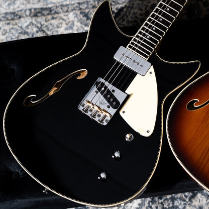 A close-up of a black Duocata guitar with checkerboard trim, a cream pickguard, and chrome hardware.