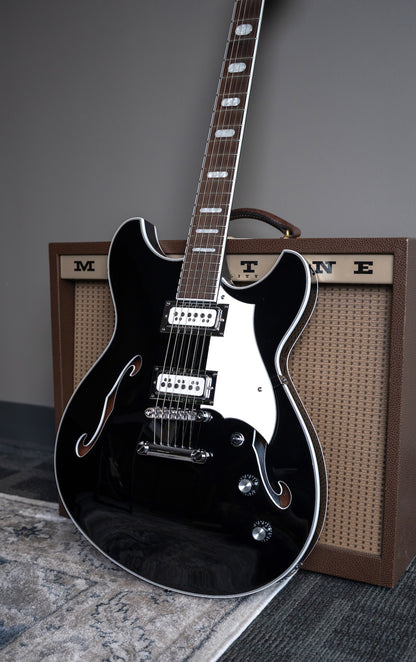 A black Regata guitar with a glossy finish and white pickguard, leaning against a brown MAGNATONE amp 