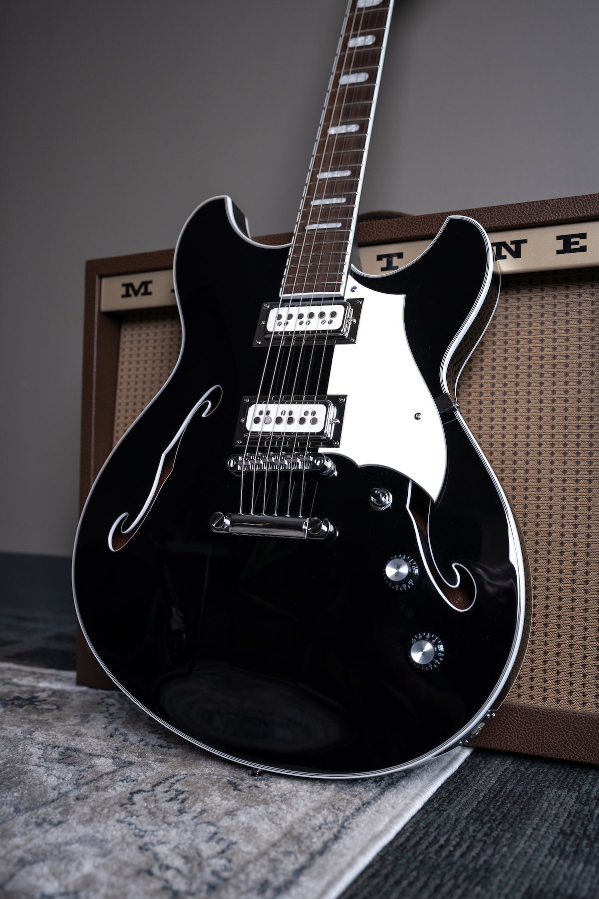 A glossy black Regata LTD double-cutaway guitar with chrome hardware, leaning against a Magnatone guitar amp.