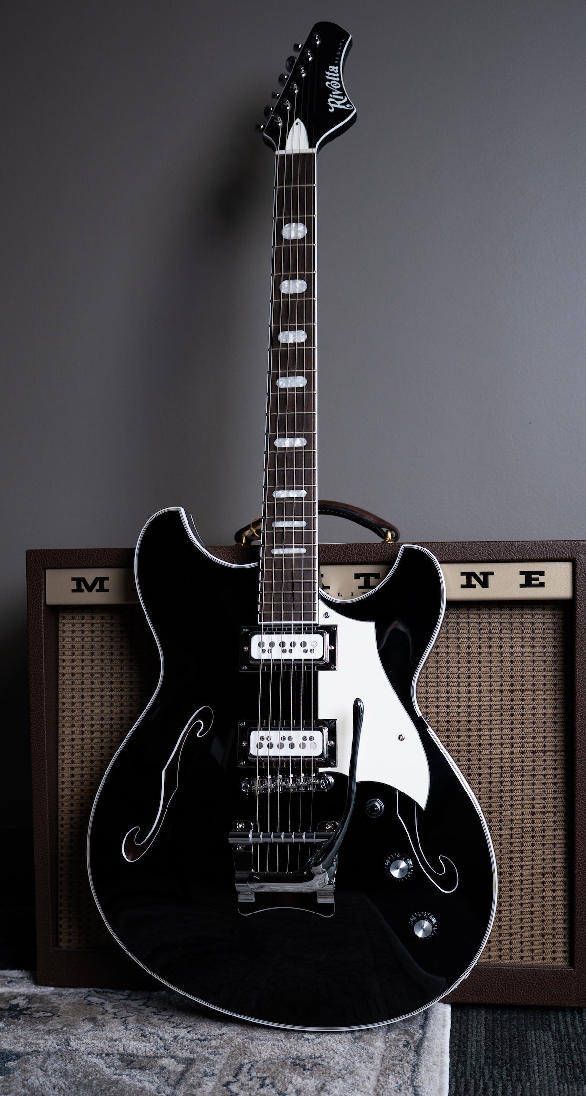 A black Regata LTD semi hollow body guitar with chrome hardware, and a Mosby Tremolo. Standing upright in front of a Magnatone guitar amplifier.